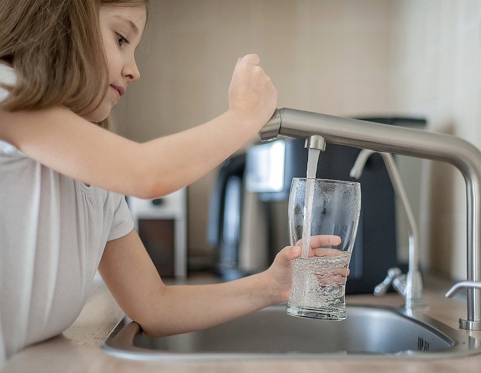 Mädchen füllt Wasser aus dem Wasserhahn ins Glas.