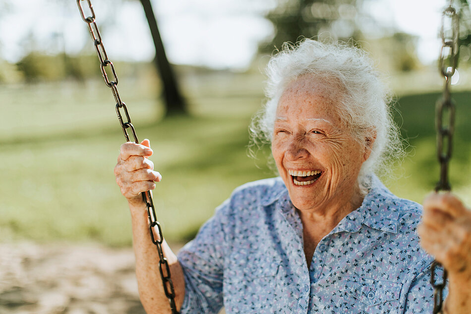 Ältere Frau sitzt auf einer Schaukel und lacht