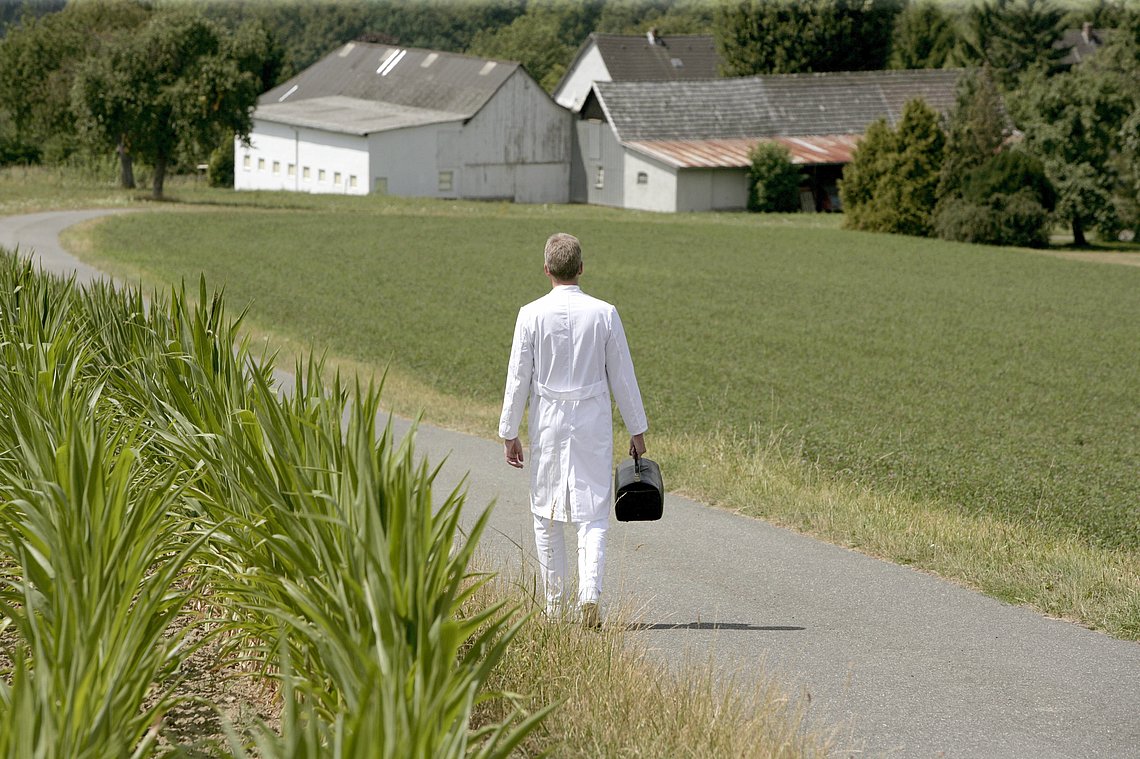 Landarzt geht durch die Felder zu einem Bauernhof