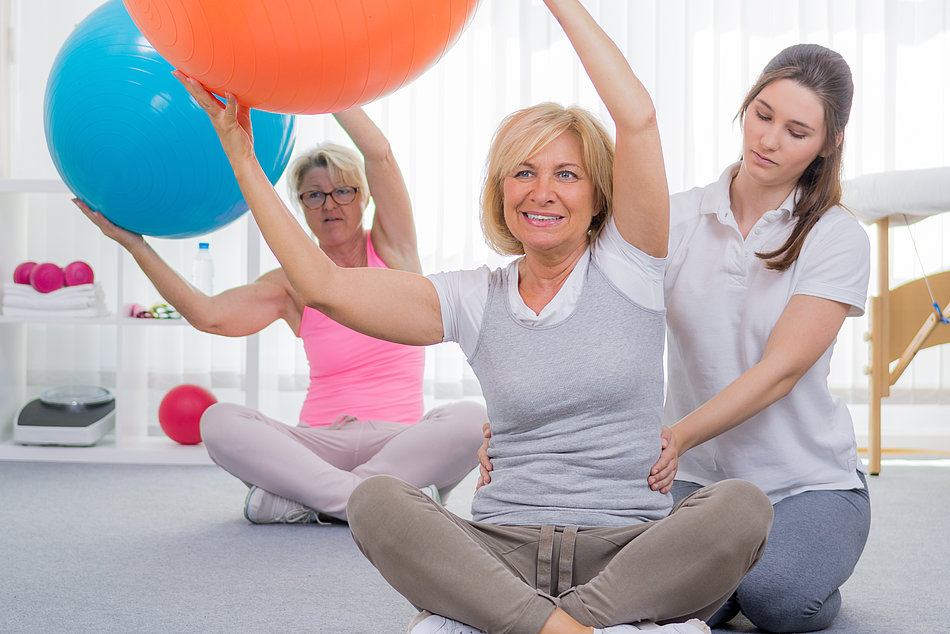 Patient macht unter Anleitung Rückenübungen mit dem Gymnastikball