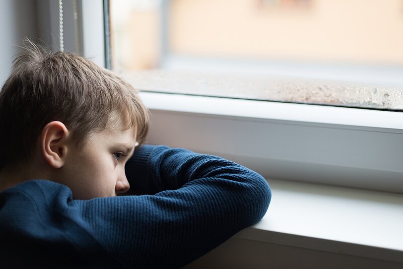 Trauriger Junge sitzt am Fenster und schaut raus