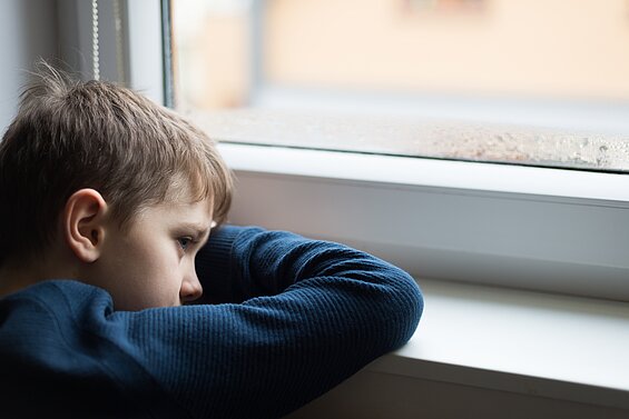 Trauriger Junge sitzt am Fenster und schaut raus