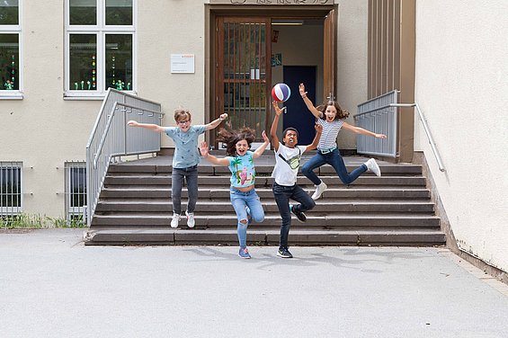 Kinder springen vergnügt die Schultreppe zum Schulhof hinunter