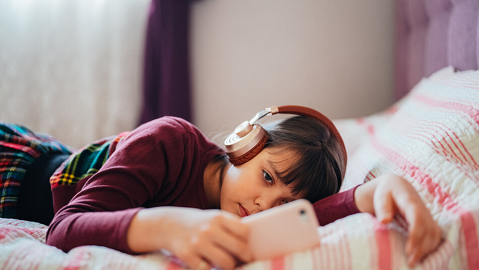 Mädchen liegt auf dem Bett und hört mit Köpfhörern Musik