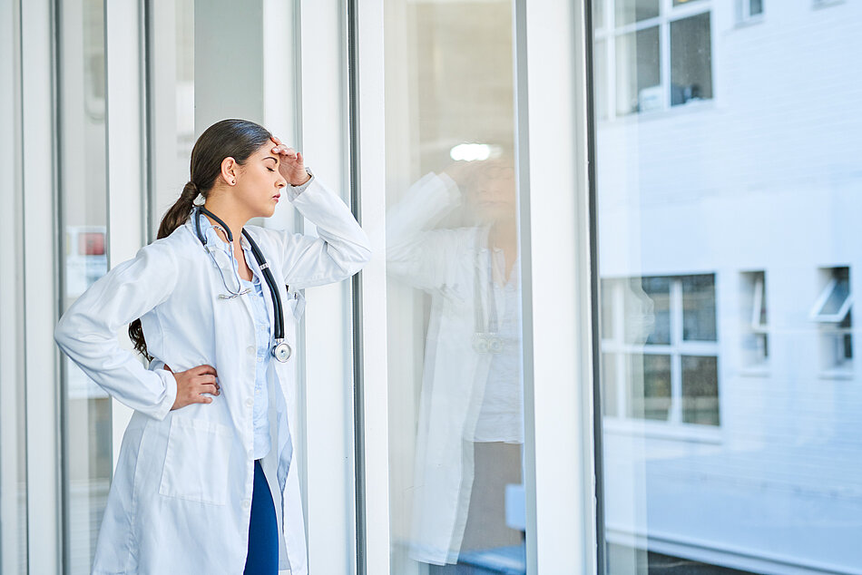 Ärztin lehnt erschöpft am Fenster