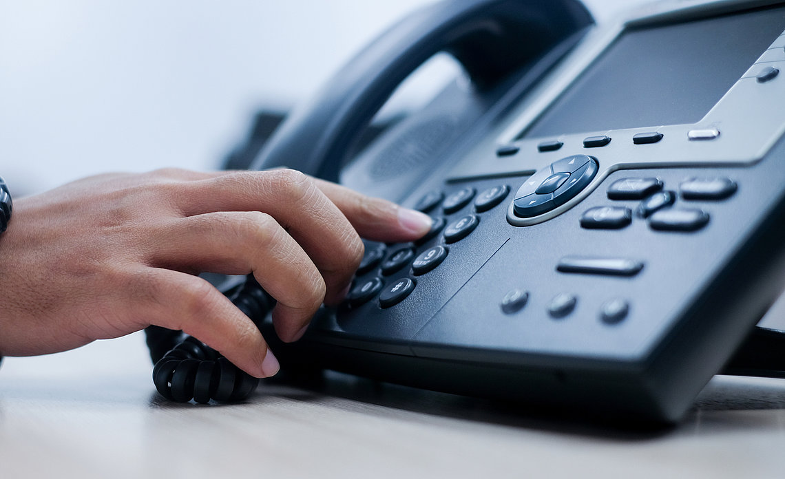 hand-am-telefon.jpg Hand eines Mitarbeiters greift zum Telefon