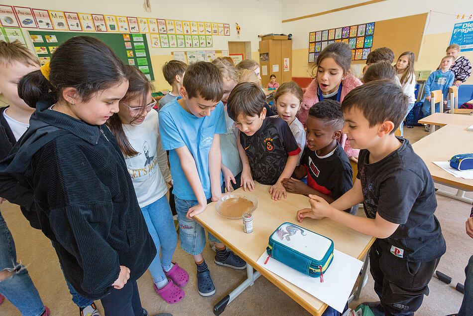 Schülerinnen und Schüler einer Grundschule stehen um einen Tisch 